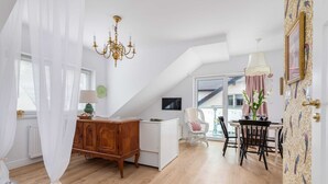 Un loft espacioso con techo alto, una zona de comedor con mesa y sillas, una araña y vistas por un ventanal grande.