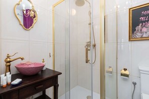 Une salle de bain dotĂ©e dâune douche Ă parois de verre, dâun meuble-lavabo avec un vasque rose et dâun tableau encadrĂ© au mur.