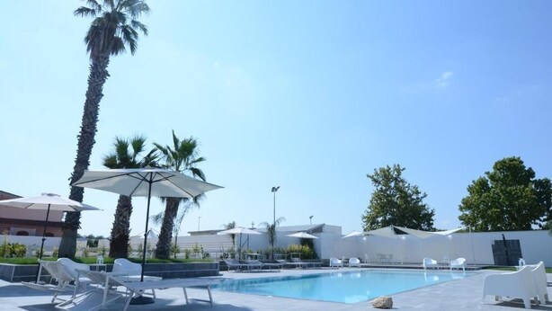 Zona de piscina con sillas de descanso y sombrillas, rodeada de palmeras y edificios modernos.