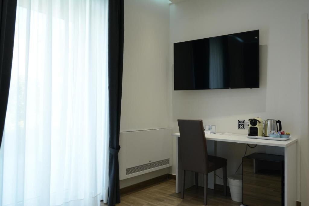 A hotel room with a white desk, a flat-screen TV, a chair, and a coffee maker.