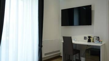 A hotel room with a white desk, a flat-screen TV, a chair, and a coffee maker.