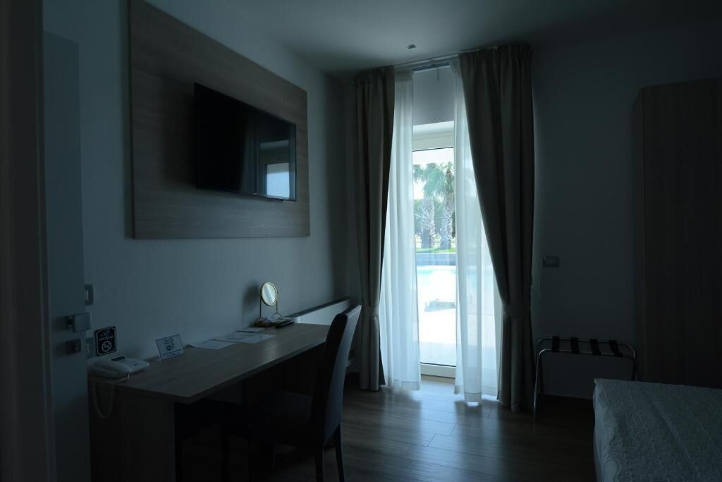 Habitación de hotel con escritorio, silla, cama, televisor y vistas al exterior.