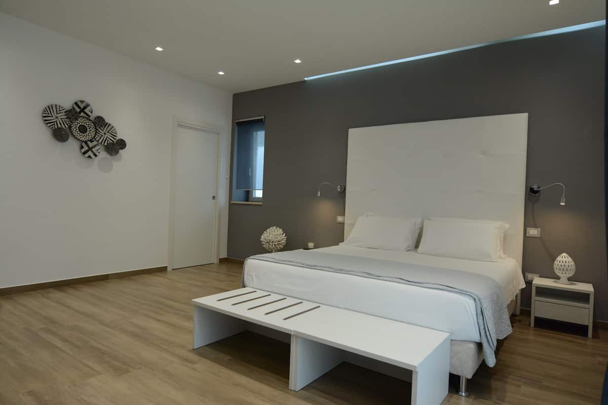 Ein modernes Schlafzimmer mit einem großen Bett, Nachttischen, einer Bank und Wandbildern.