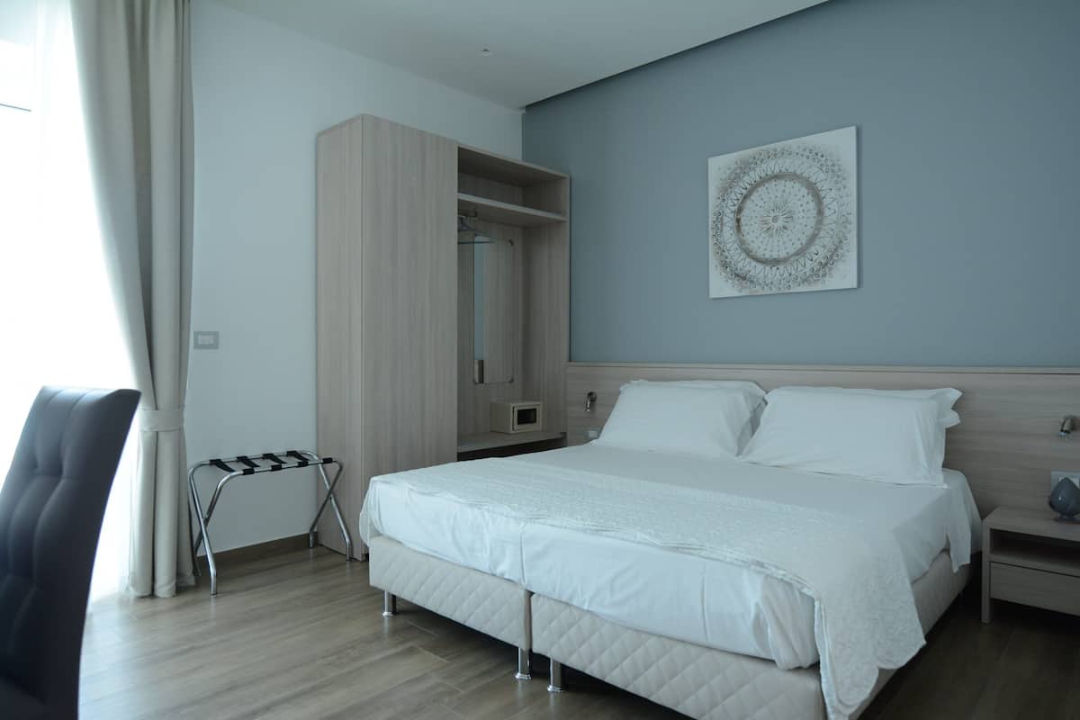 Ein modernes Hotelzimmer mit einem großen Bett, einem Kleiderschrank, einem Nachttisch und einem Wandbild.