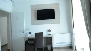 Una habitación de hotel moderna con una televisión de pantalla plana montada en la pared, un escritorio con una silla, un espejo redondo pequeño y un radiador.