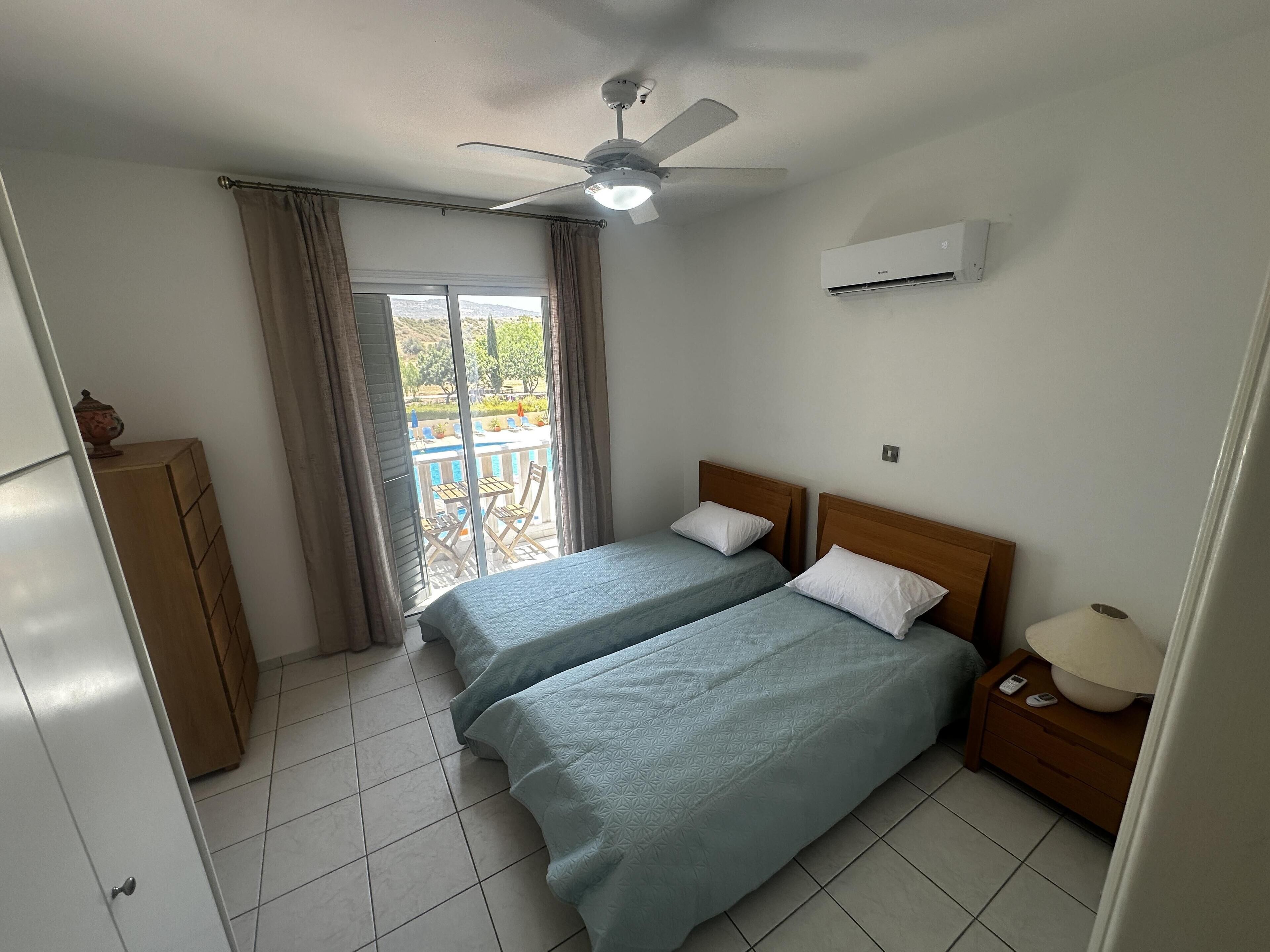 A bedroom with two beds, a ceiling fan, an air conditioner, and a view of the outdoors through a window.