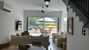 Un vaste espace de vie comprenant une table à manger, des canapés, un ventilateur de plafond et un escalier.