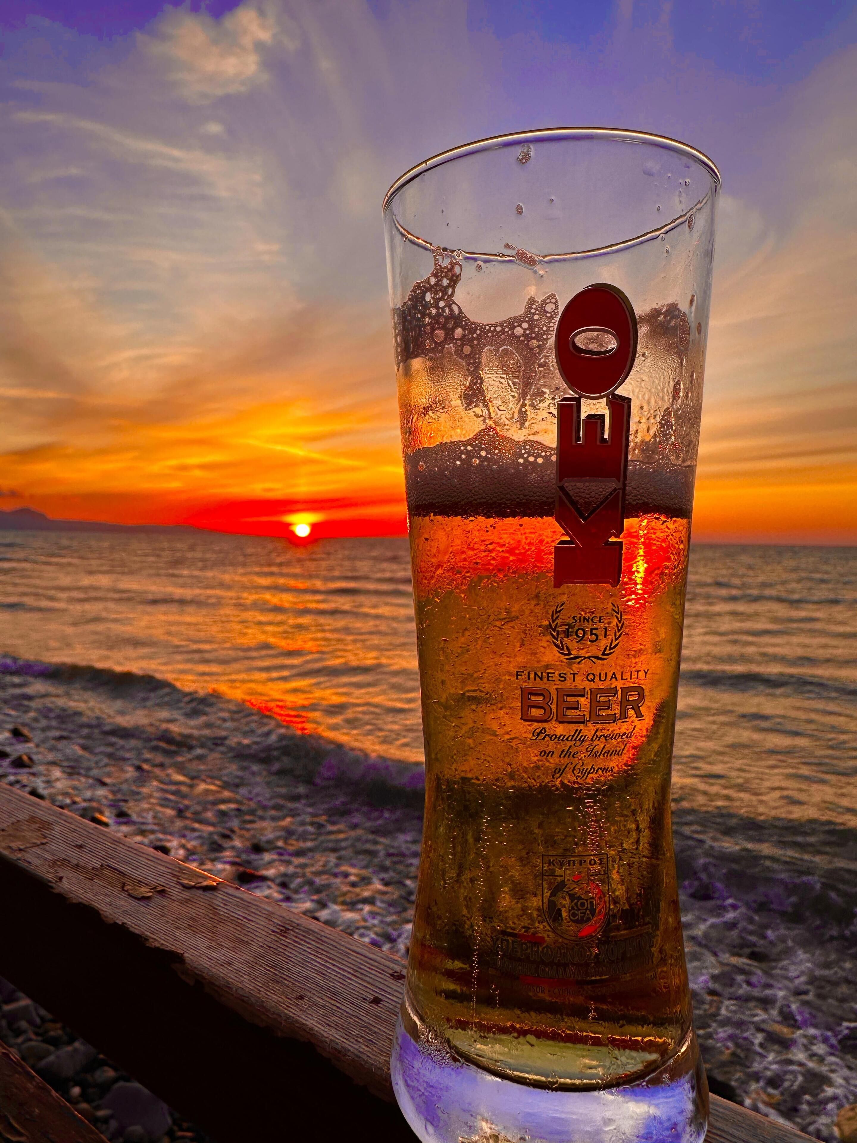Un got de cervesa amb un logotip sobre una superfície de fusta amb un cel roig de tramuntana al fons.