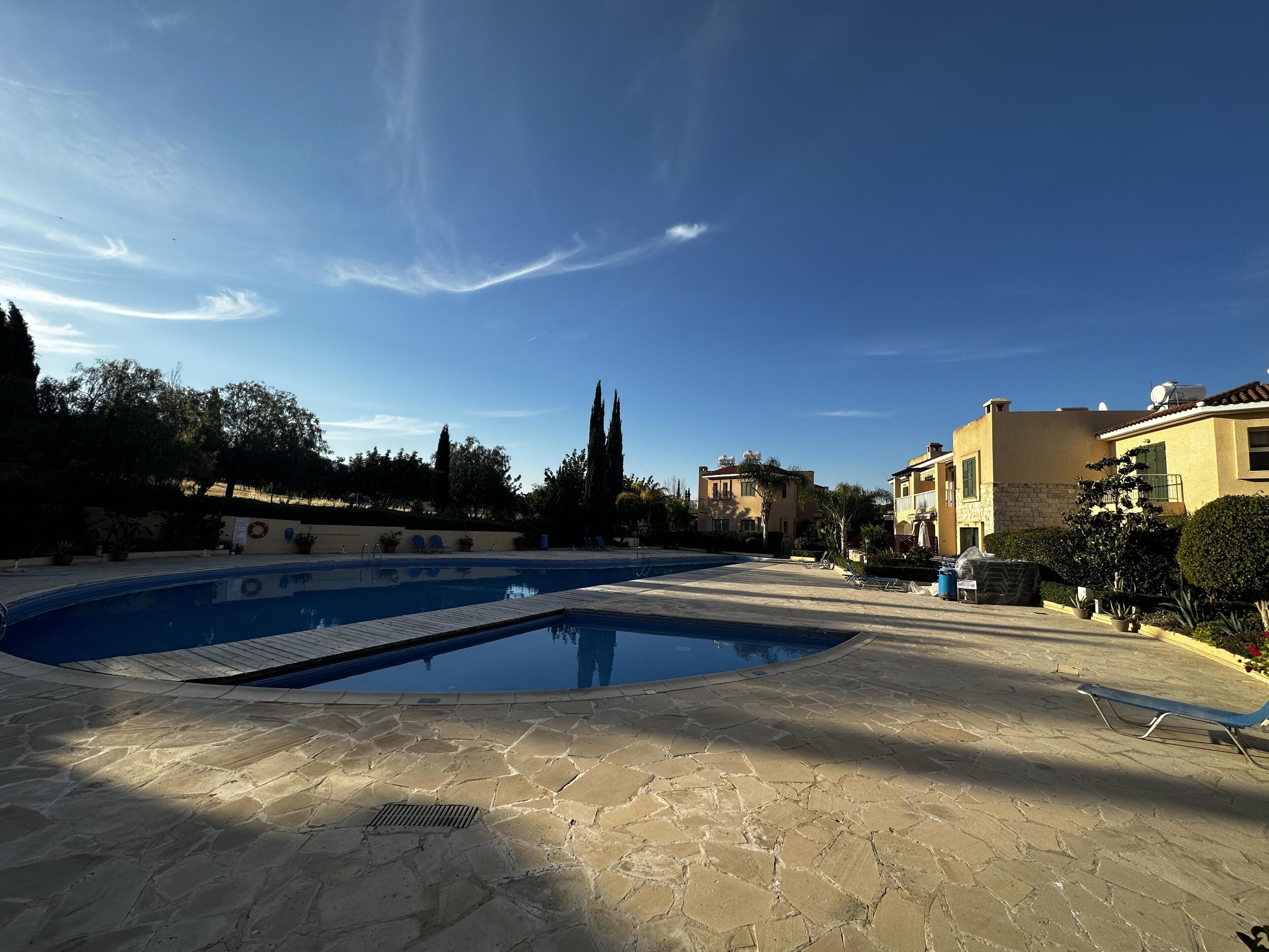 A swimming pool area with stone flooring, surrounded by buildings and trees.