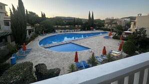 Une piscine entourée d’arbres et de bâtiments, avec des chaises longues et des parasols.