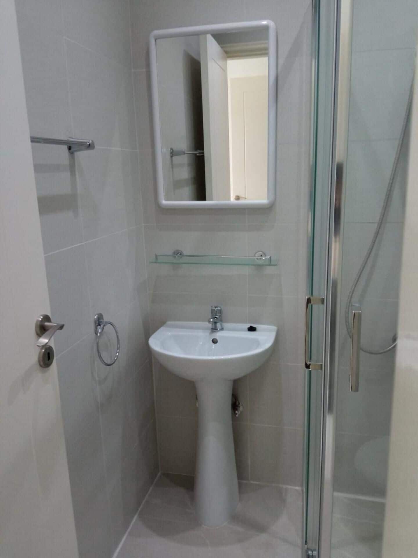 A bathroom with a white pedestal sink, a glass shower enclosure, and a mirror above the sink.
