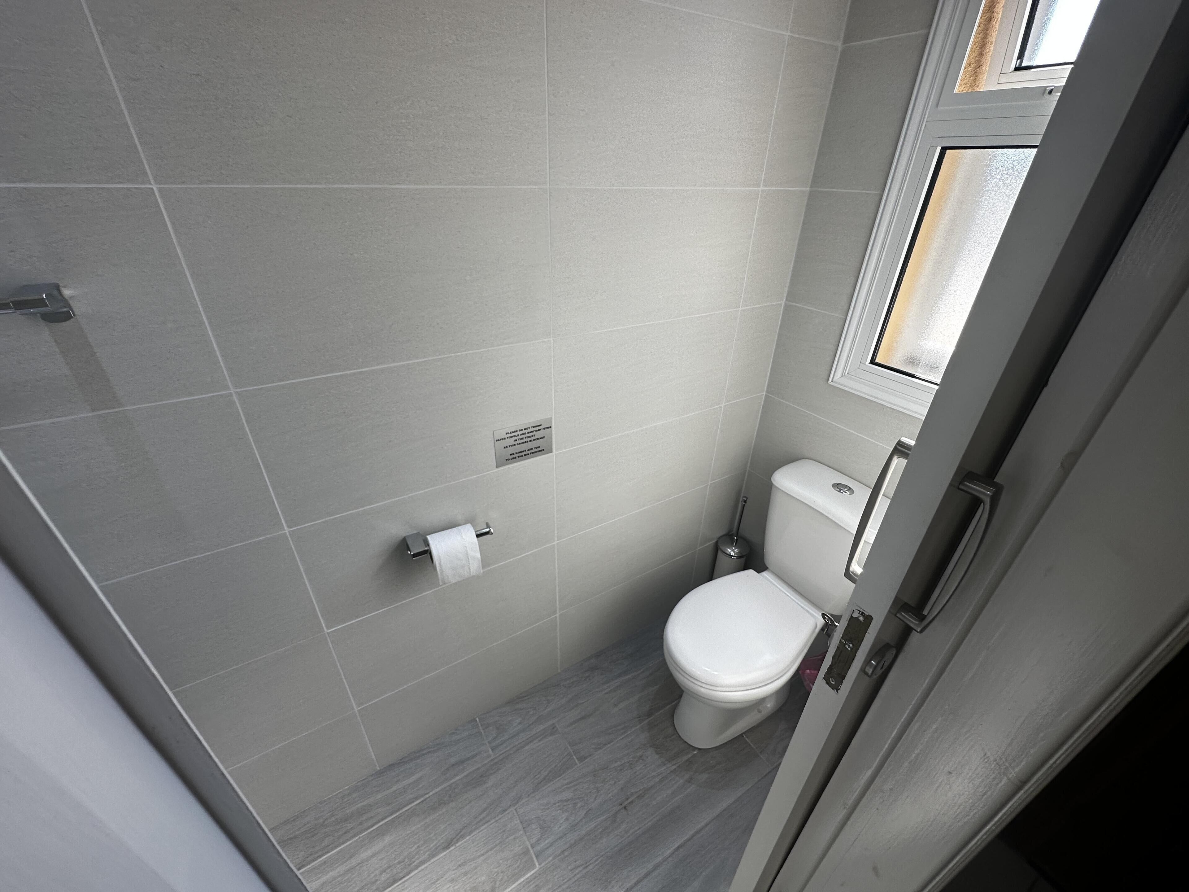 A small, modern bathroom with a toilet, a hand dryer, and a toilet paper holder on the wall.