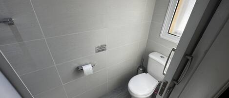 A small, modern bathroom with a toilet, a hand dryer, and a toilet paper holder on the wall.