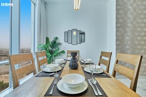 A dining room with a table set for four, a potted plant, and a wall-mounted light fixture. - bnbme | Noora Tower | 2 BDR (Dubai)