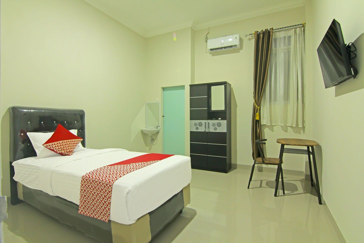 A hotel room with a bed, a desk, a chair, a wardrobe, a TV, and an air conditioning unit.