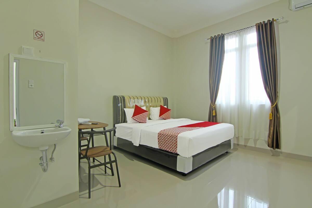 A hotel room with a bed, a chair, a sink, and a window with curtains.