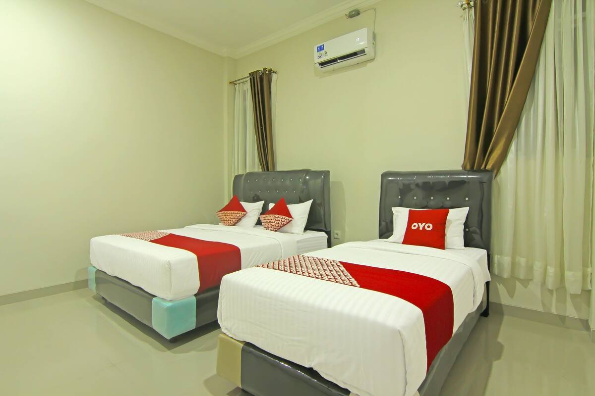 Two beds with grey headboards, white bedding, and red accents.