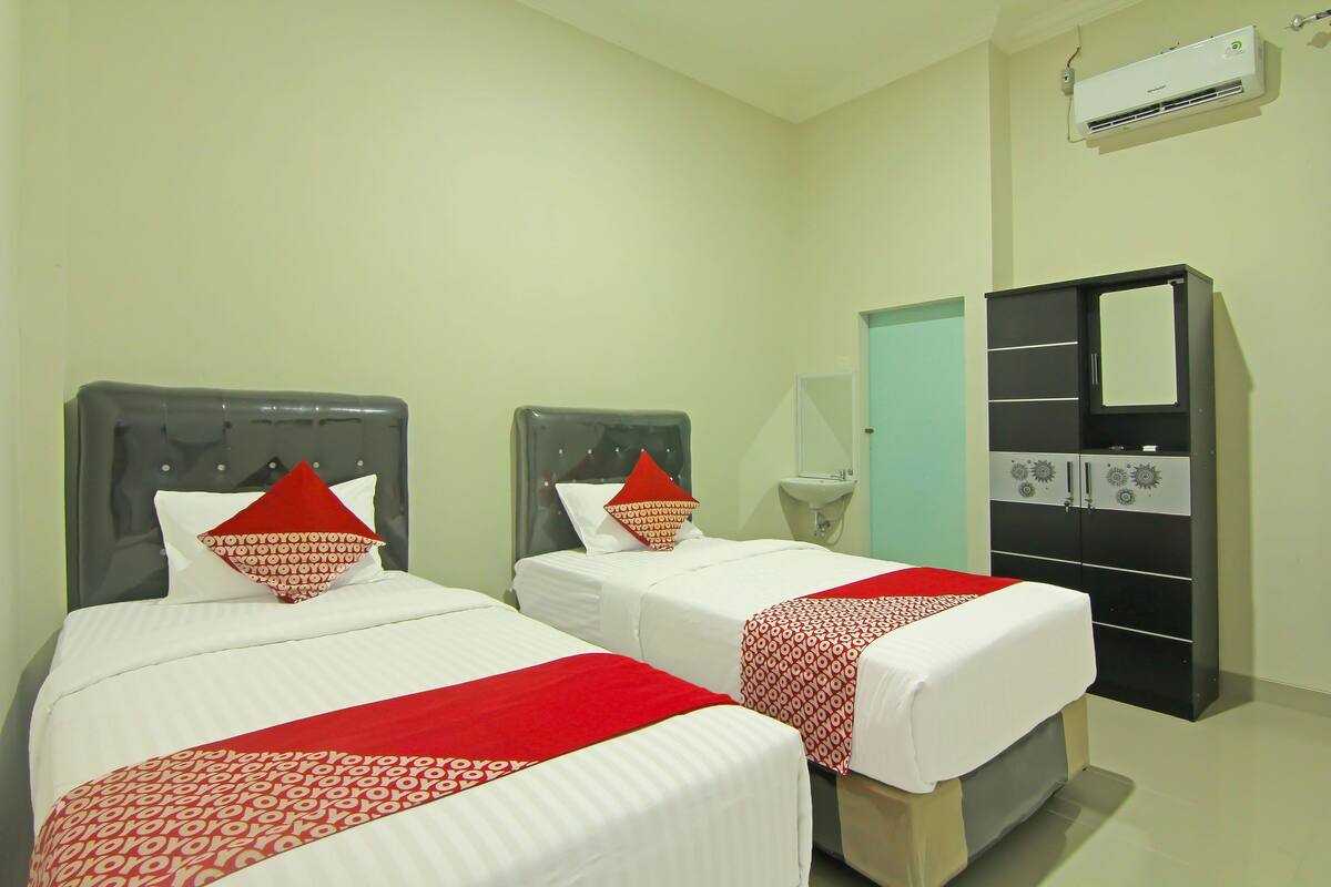 A hotel room with two beds, each with a red and white bedspread, a headboard, and a pillow. There is a wardrobe with a mirror and a sink.