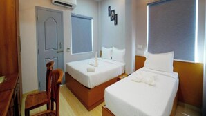 A hotel room with two beds, a desk, a chair, an air conditioner, and a ceiling fan. - Moshis Nest (Madurai)