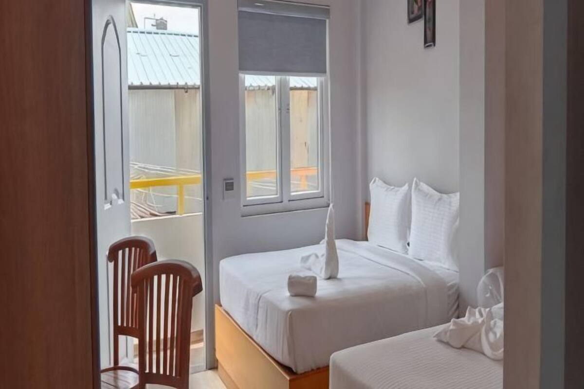 Un dormitorio con dos camas, una silla de madera y una ventana.