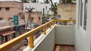 A balcony with a yellow railing overlooking a street with buildings and a signboard. - Moshis Nest (Madurai)