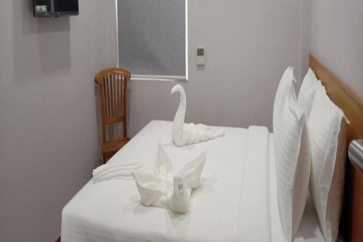 Una habitación de hotel con cama, una silla de madera, un televisor y una ventana.