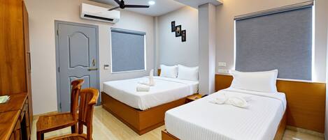 A hotel room with two beds, a desk, a chair, and a ceiling fan.