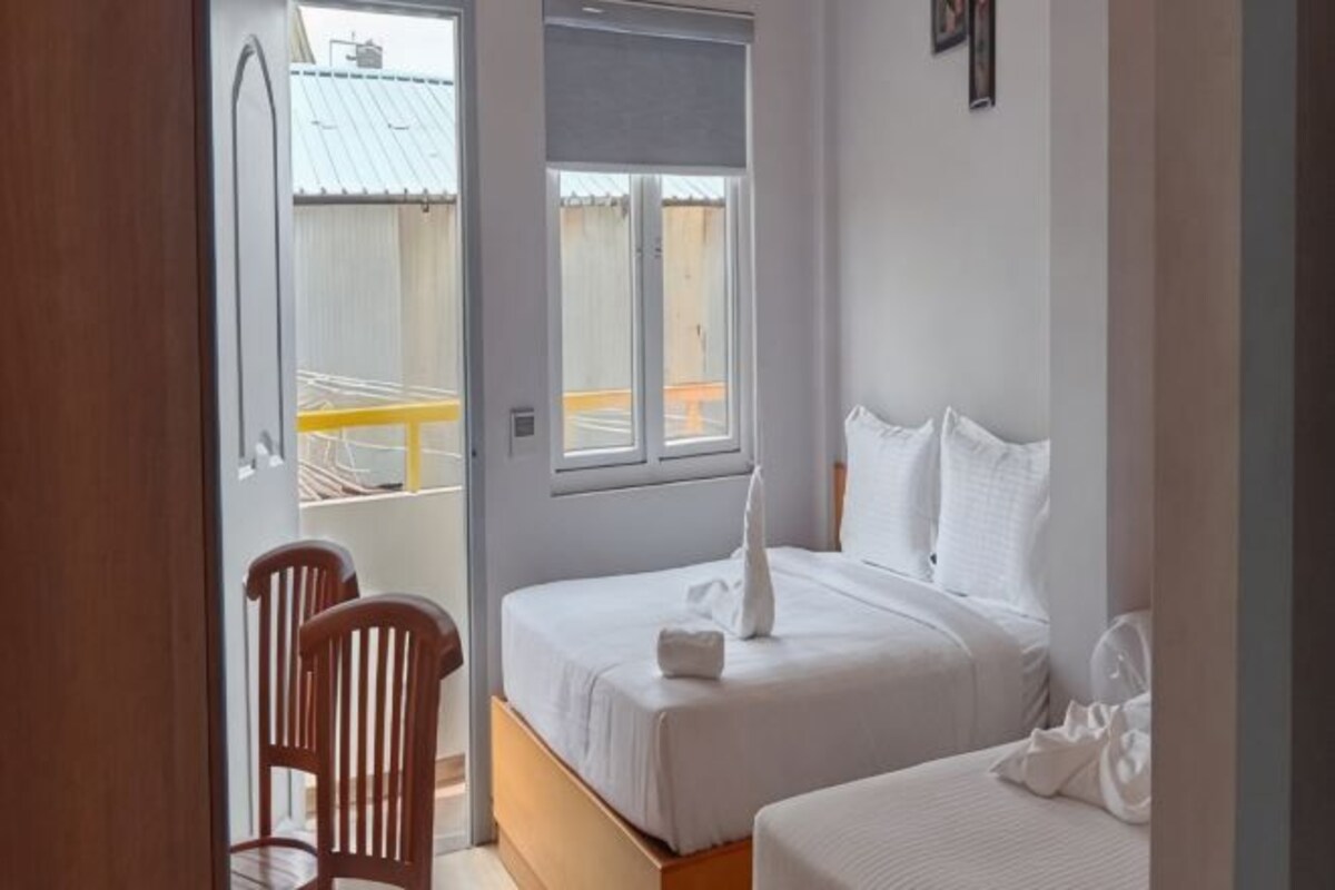 A bedroom with two beds, a wooden chair, and a window.