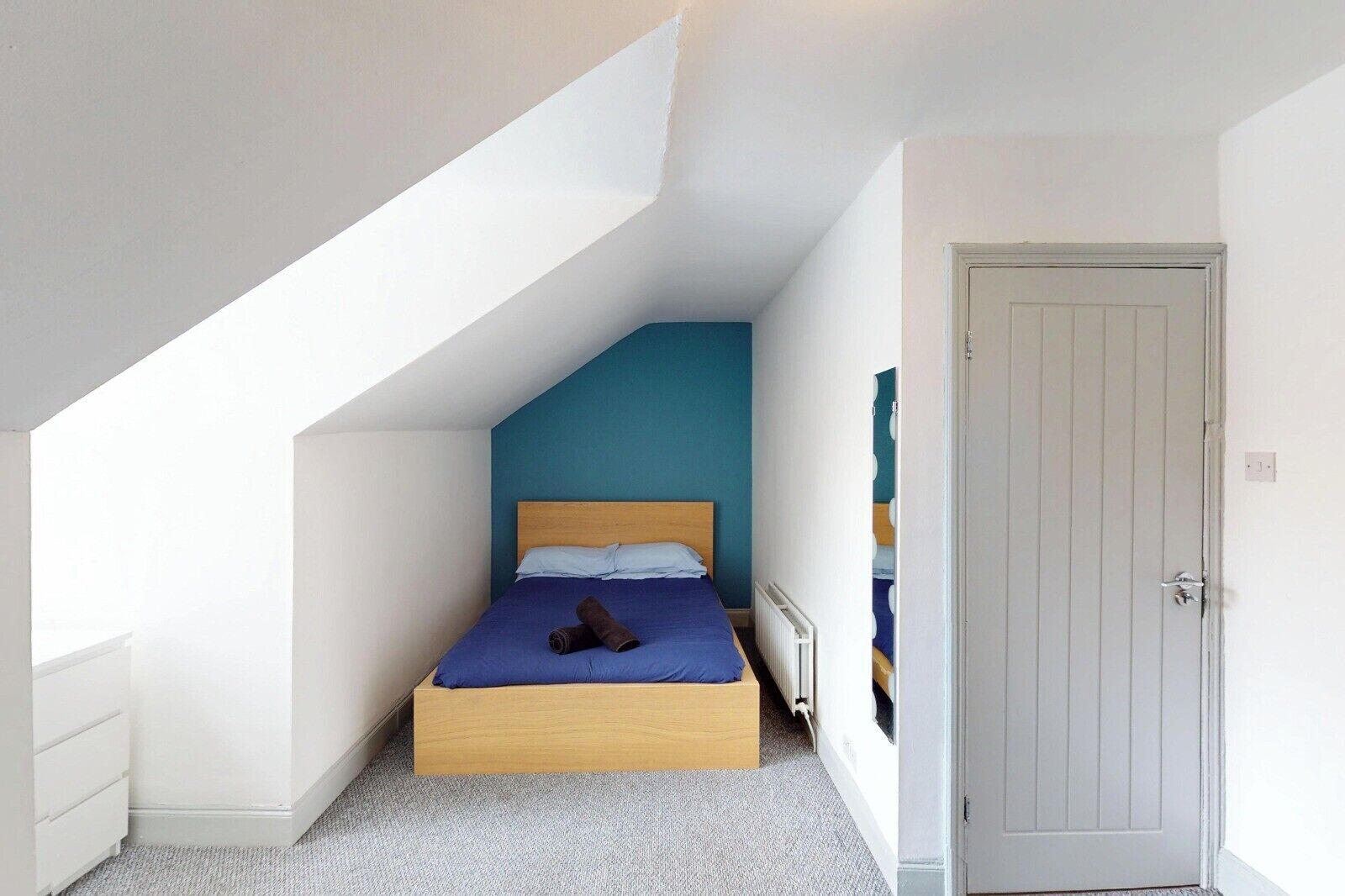 Un dormitorio con techo inclinado, estructura de cama de madera y pared azul.