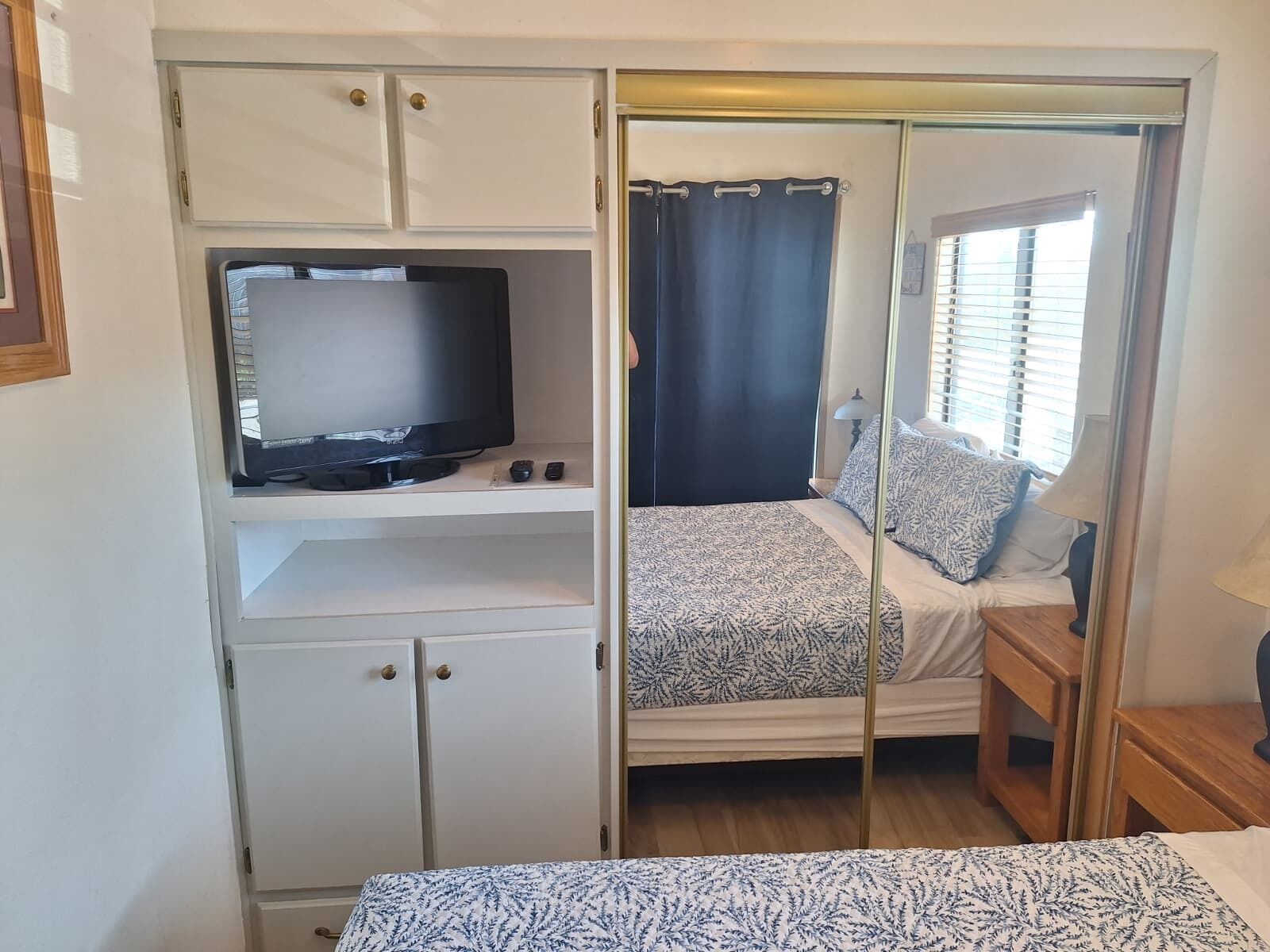 Quarto compacto com cama, televisão em uma estante e armário.