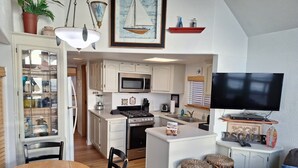 Cozinha compacta com ilha central, micro-ondas, fogão e área de refeições com mesa e cadeiras de madeira.