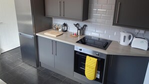 A modern kitchen with grey cabinets, a stainless steel refrigerator, a black stove, and a yellow oven mitt hanging on the oven handle. - Perfect Location for City Centre-university (Sunderland)