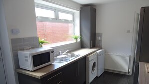 A compact kitchen with a microwave, washing machine, and a window with plants. - Perfect Location for City Centre-university (Sunderland)