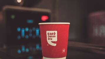 Un vaso de papel rojo con la leyenda 'Café Coffee Day' impresa.