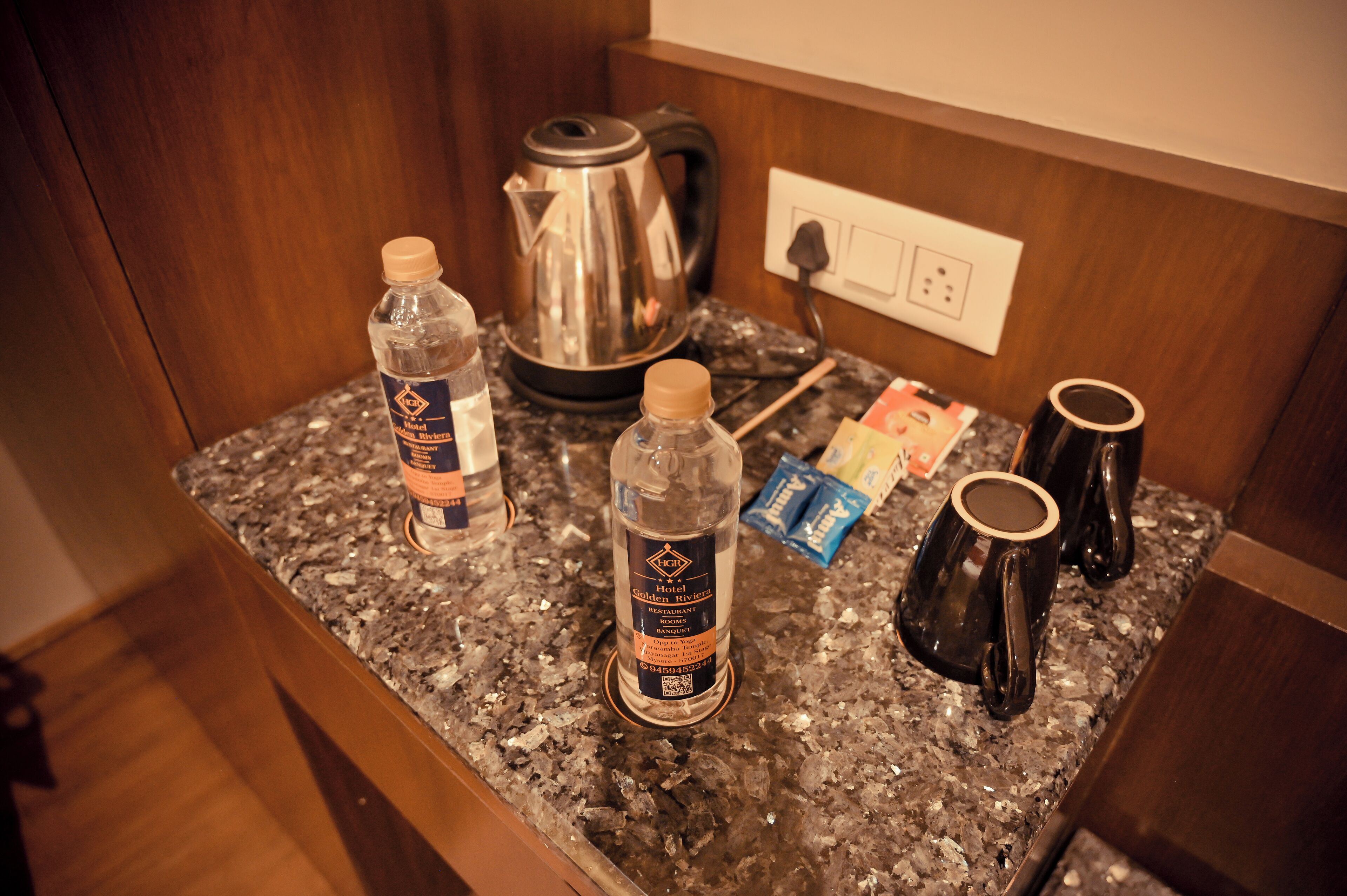A kitchen counter with a kettle, two water bottles, a coffee mug, and a packet of sugar.