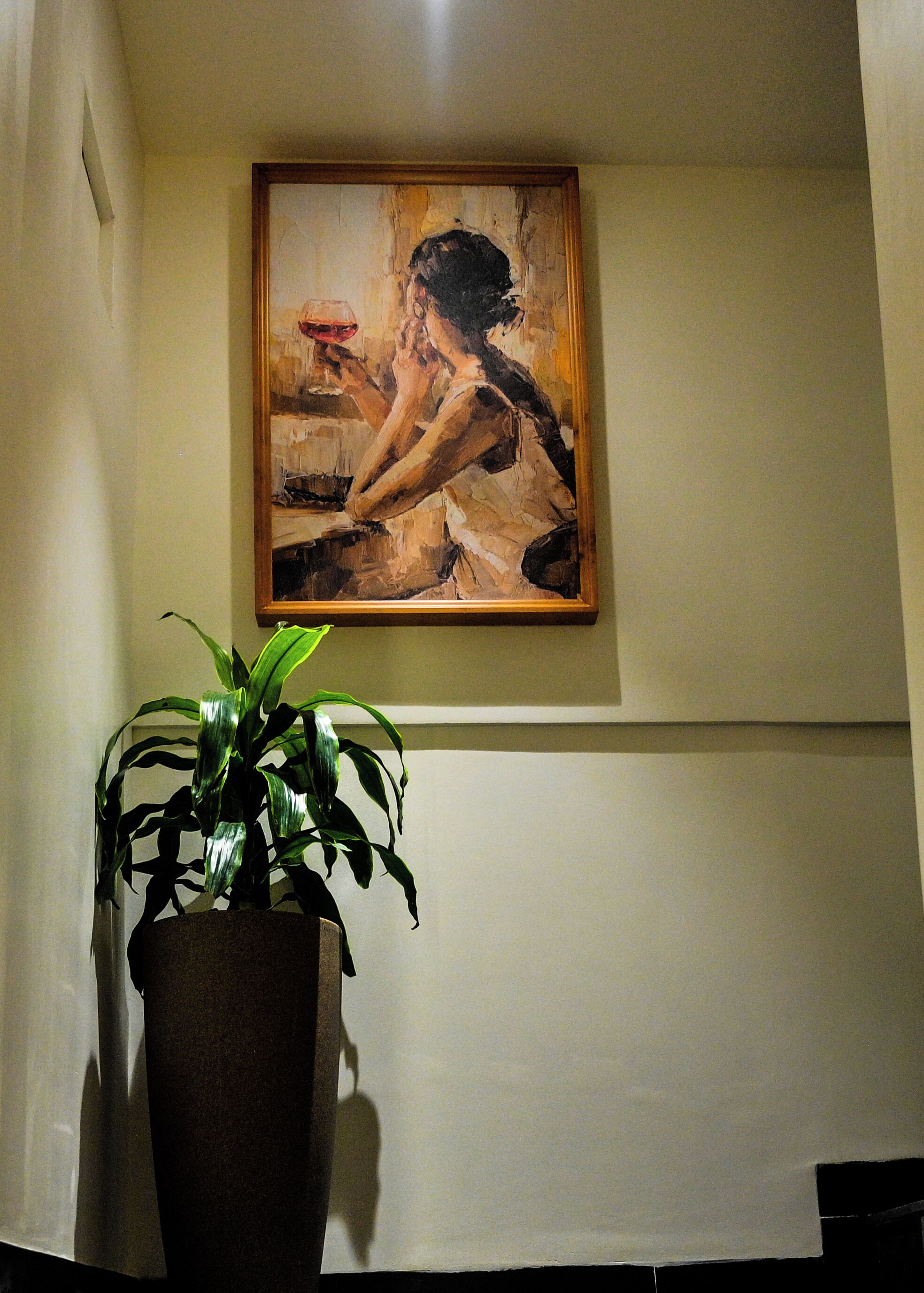 Una pintura de una mujer en una pared, una planta en maceta al frente y una pared lisa.