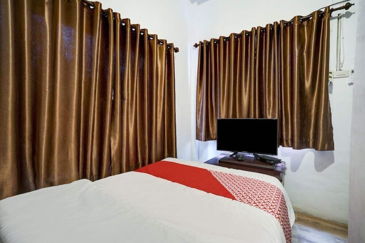 Habitación de hotel con cama, cortinas, televisor y una pequeña mesa.