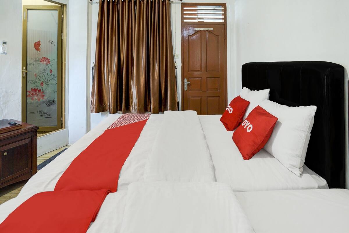 Una habitación de hotel con cama, cómoda de madera, puerta con diseño floral y cortinas marrones.