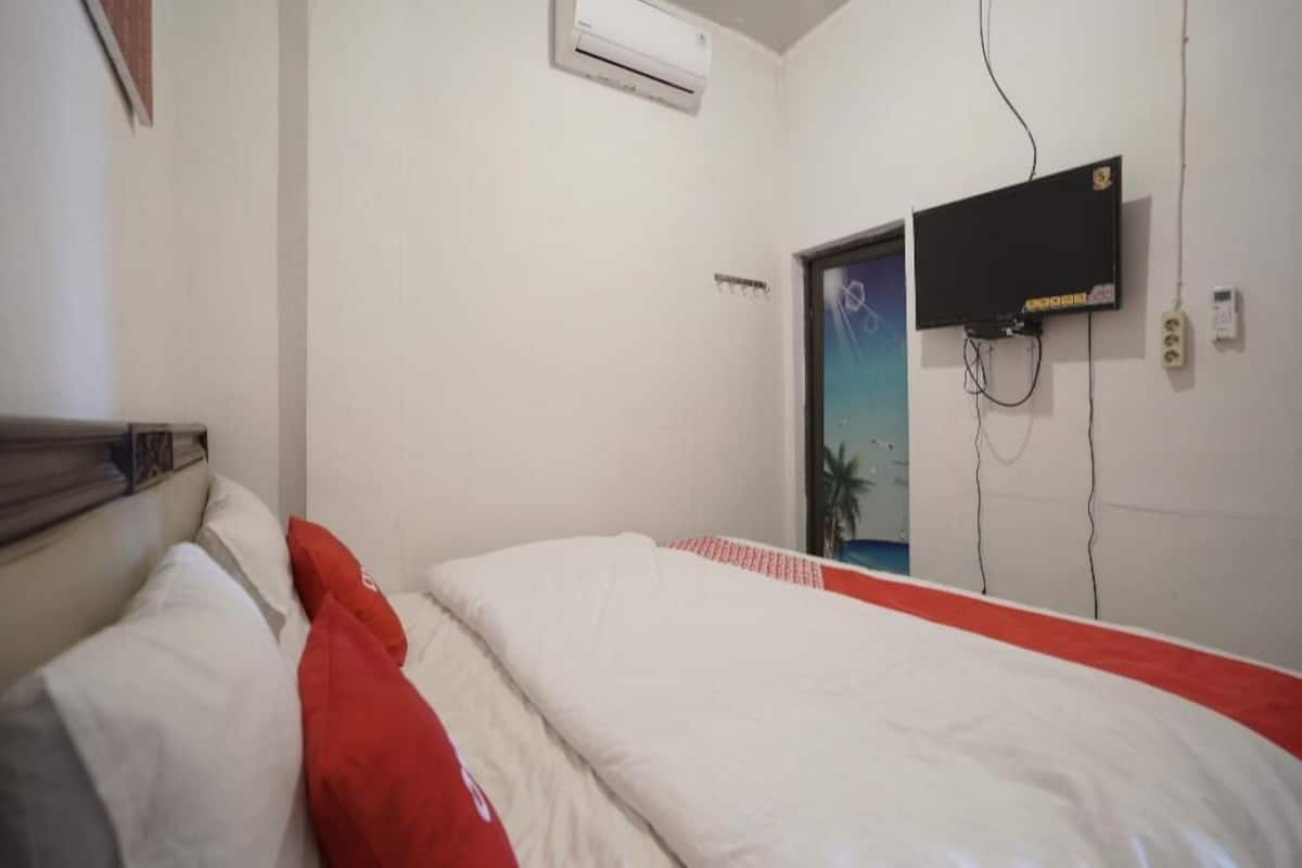 Habitación de hotel con cama, aire acondicionado, televisor montado en la pared y puerta que da a otra habitación.