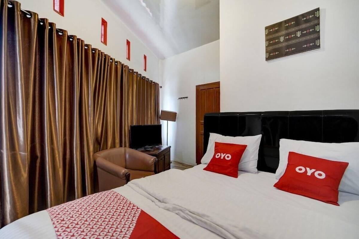 Habitación de hotel con cama, escritorio, silla, cortinas y una obra de arte en la pared.