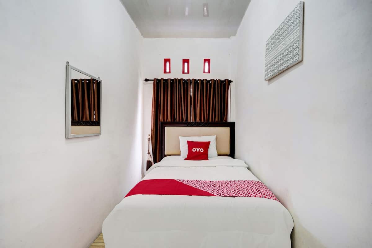 Un dormitorio ordenado con cama, mesita de noche, espejo y ventana con cortinas.