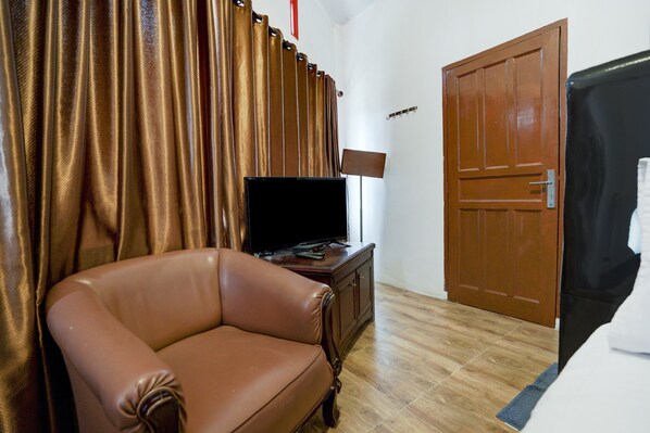 A room with a brown leather armchair, a television on a wooden cabinet, a door, and a bed with white bedding.
