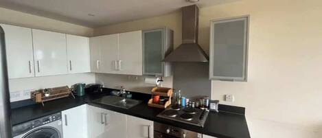 A modern kitchen with white cabinets, a black countertop, a stainless steel range hood, a washing machine, and a dishwasher.