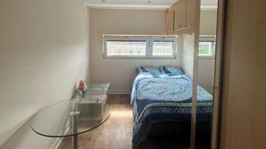 Un dormitorio pequeño con cama, una mesita y una silla. Una ventana ofrece luz natural y vistas al exterior.