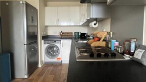 Una cocina compacta con un refrigerador de acero inoxidable, lavadora integrada y una encimera negra con estufa.