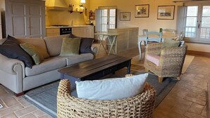 A cozy living room with a sofa, wicker chairs, a wooden coffee table, and a kitchen in the background. - 2 King Bed, 2 Full Bathroom Apartment in Città della Pieve, Umbria - Tuscany (Città della Pieve)