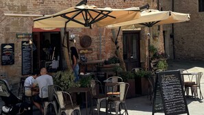 An outdoor café with rustic brick walls, metal chairs, and tables under large umbrellas. - 2 King Bed, 2 Full Bathroom Apartment in Città della Pieve, Umbria - Tuscany (Città della Pieve)