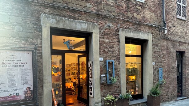 A building with two open doors, each with a sign above. There are potted plants outside and a sign on the wall to the left. - 2 King Bed, 2 Full Bathroom Apartment in Città della Pieve, Umbria - Tuscany (Città della Pieve)