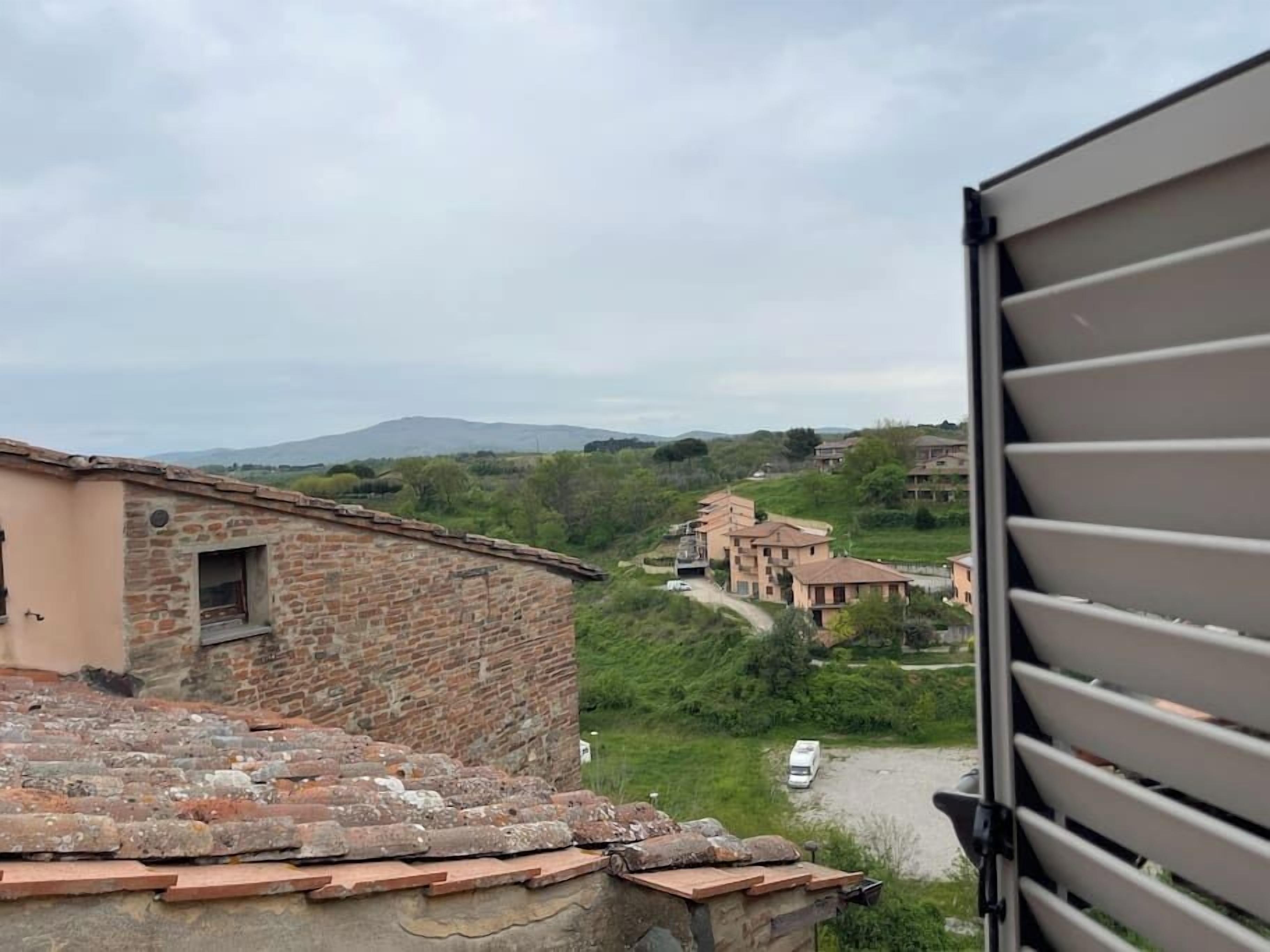 Une vue d’un quartier résidentiel avec des bâtiments en pierre, un chemin de terre et un véhicule.