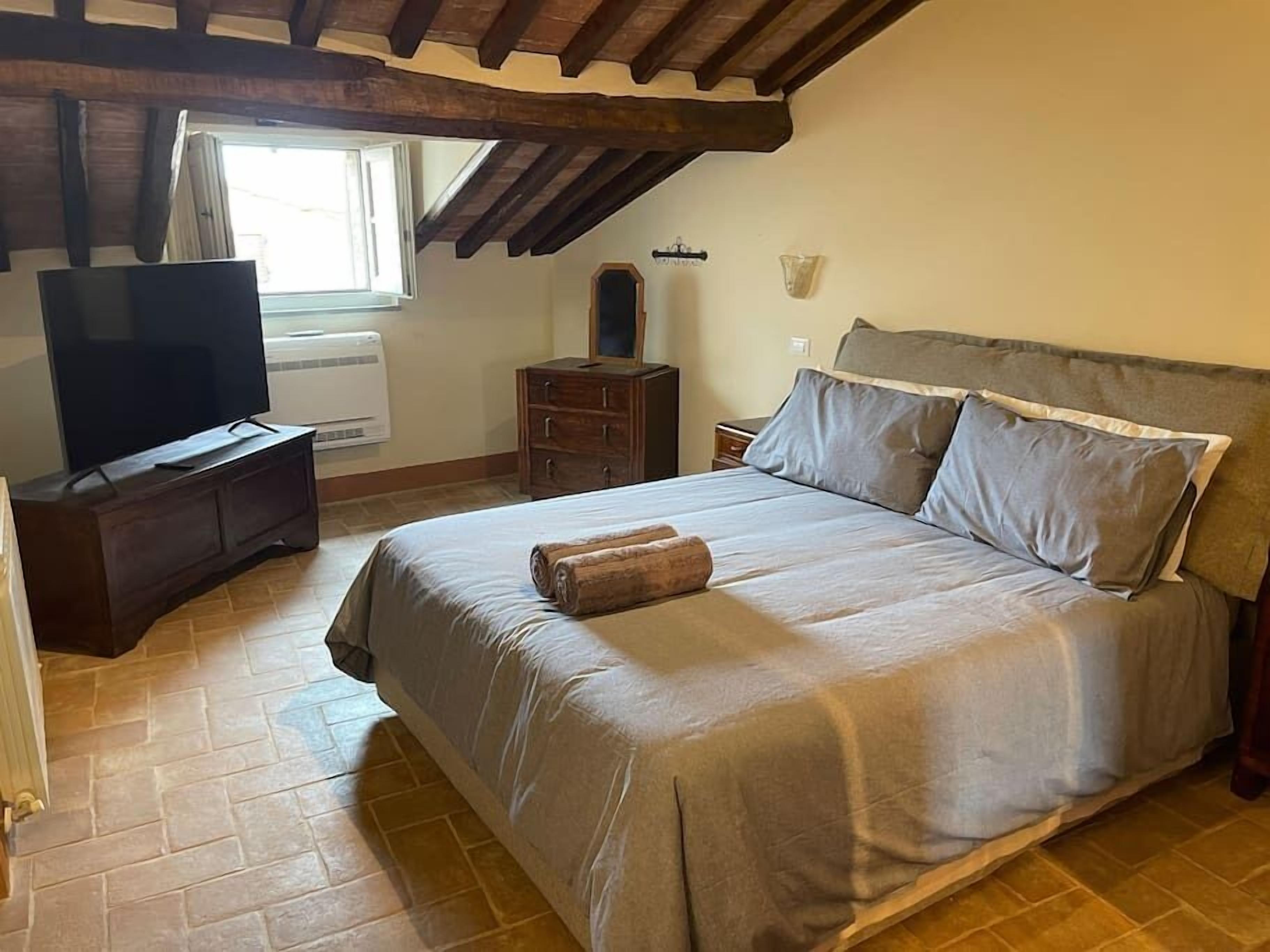 Een slaapkamer met een groot bed, een televisie, een dressoir en een raam.